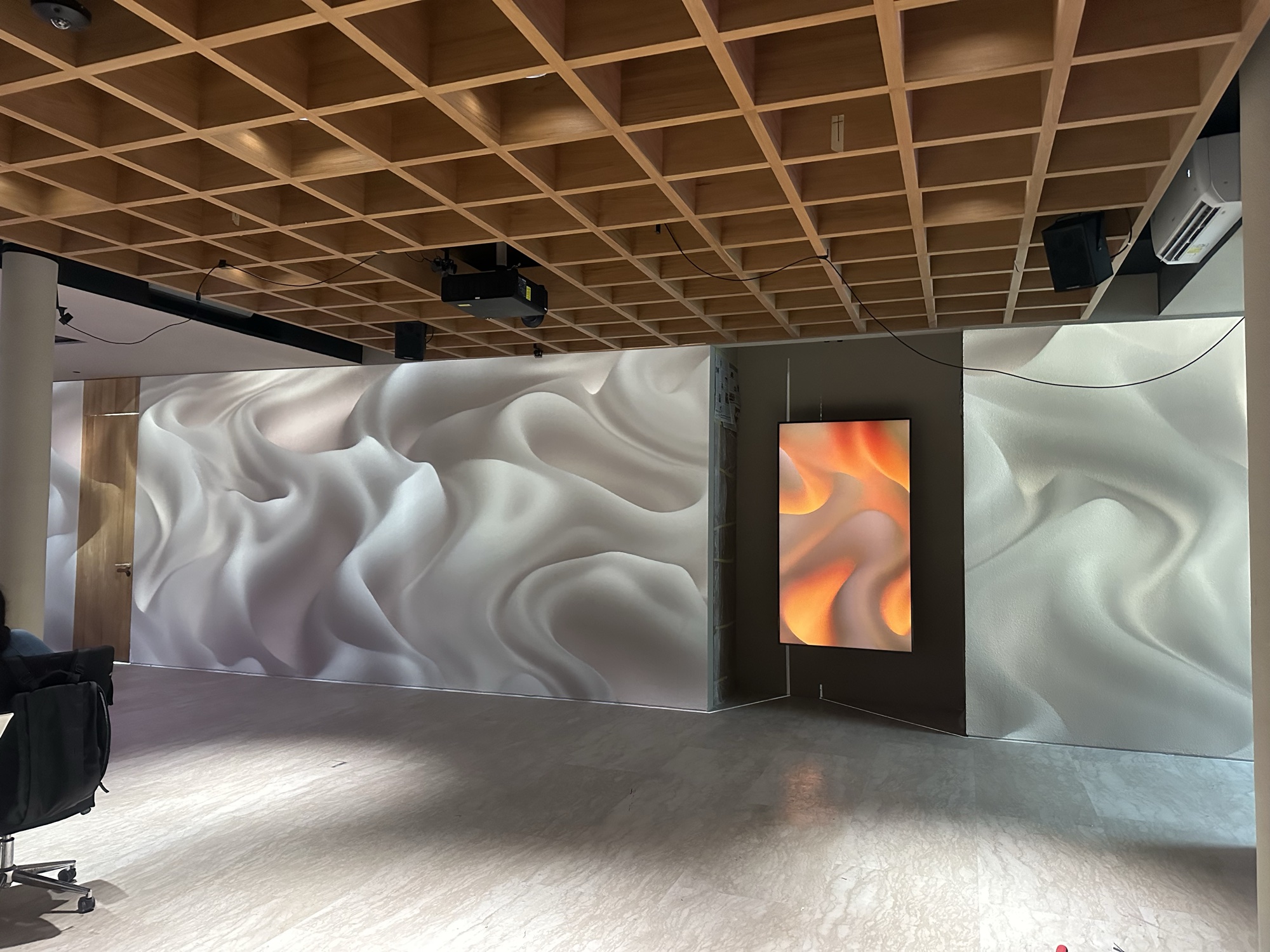 Villa Ailla living wall in commissioning — projection-mapped fluid relief across two walls, ceiling projection rig visible