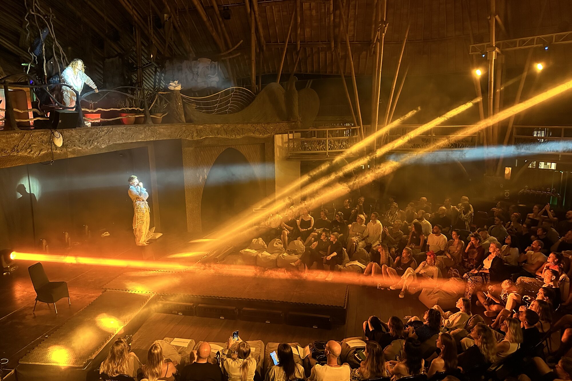 ASH Theatre — performance under warm beams, full house in the round, bamboo structure overhead